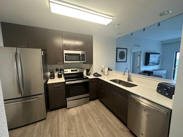 kitchen featuring sink, light hardwood / wood-style flooring, a textured ceiling, kitchen peninsula, and stainless steel appliances