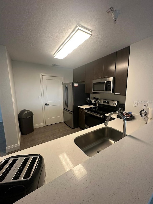 kitchen with stainless steel appliances, sink, dark wood-type flooring, and a textured ceiling