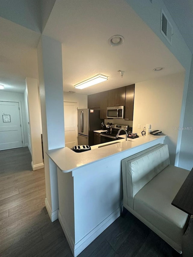 kitchen featuring a breakfast bar area, dark hardwood / wood-style flooring, gray cabinets, kitchen peninsula, and stainless steel appliances