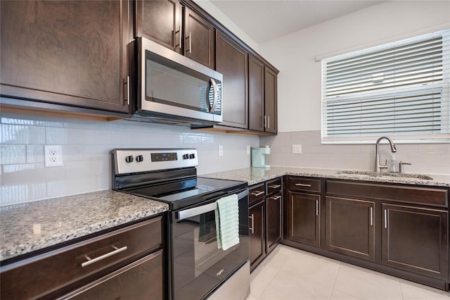 kitchen with sink, light tile patterned floors, appliances with stainless steel finishes, light stone counters, and dark brown cabinetry