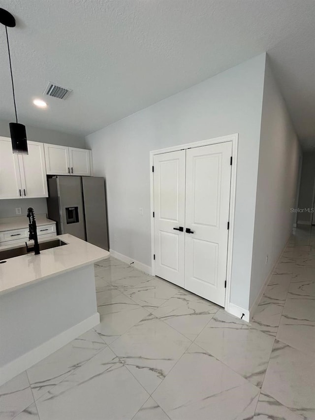 kitchen featuring sink, hanging light fixtures, stainless steel fridge, a textured ceiling, and white cabinetry