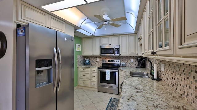 kitchen with stainless steel appliances, light stone countertops, sink, and cream cabinetry