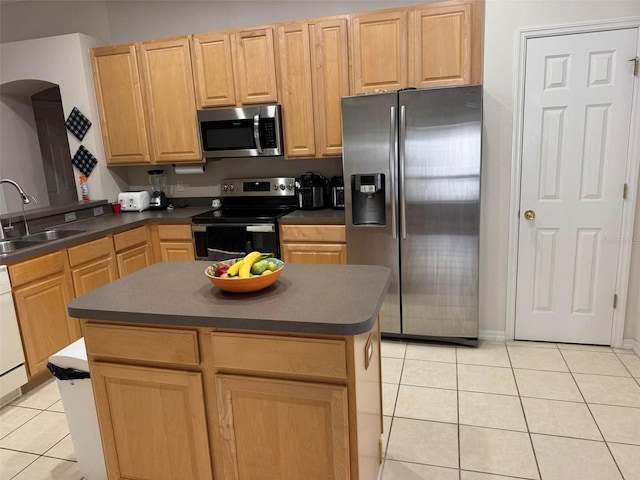 kitchen with appliances with stainless steel finishes, light tile patterned floors, light brown cabinetry, a kitchen island, and sink