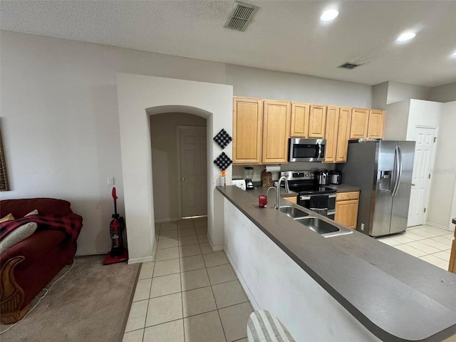 kitchen with kitchen peninsula, light brown cabinetry, light tile patterned floors, appliances with stainless steel finishes, and sink