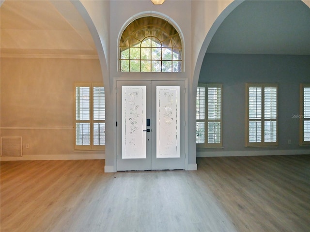 foyer entrance with wood-type flooring, ornamental molding, and french doors