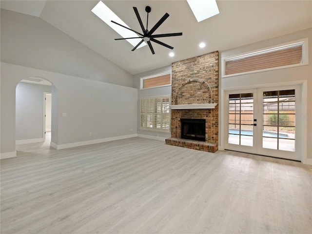 unfurnished living room featuring ceiling fan, light hardwood / wood-style flooring, high vaulted ceiling, and a brick fireplace