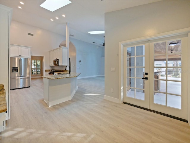 kitchen featuring appliances with stainless steel finishes, a skylight, light stone counters, ceiling fan, and white cabinetry