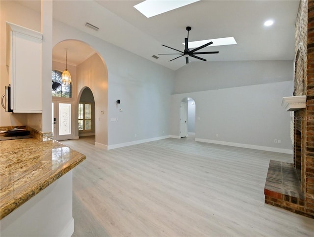 living room featuring a skylight, ceiling fan, light hardwood / wood-style flooring, high vaulted ceiling, and a fireplace