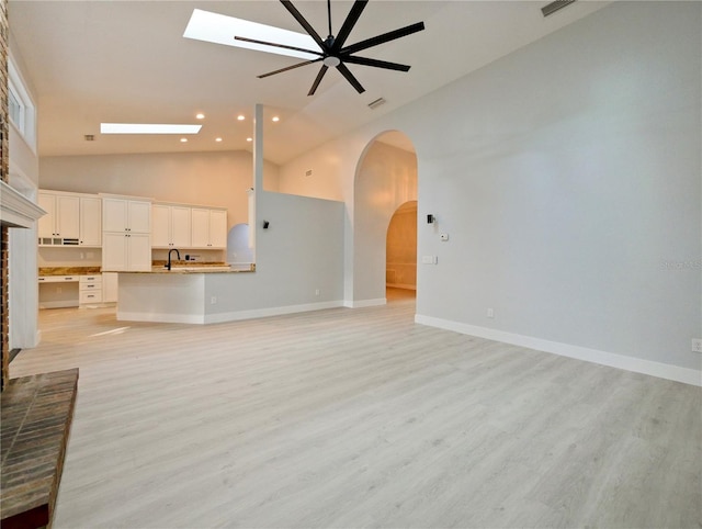 unfurnished living room with a skylight, ceiling fan, sink, light hardwood / wood-style flooring, and high vaulted ceiling