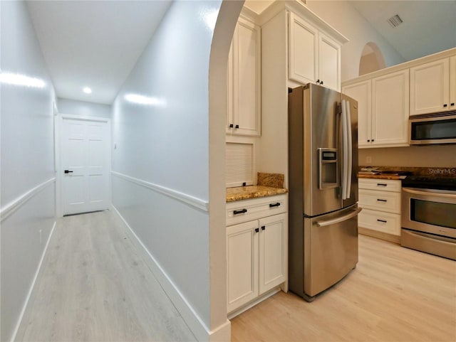 kitchen featuring light stone counters, white cabinetry, stainless steel appliances, and light hardwood / wood-style flooring