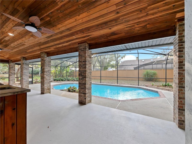 view of pool with exterior bar, glass enclosure, ceiling fan, and a patio area