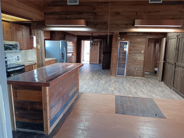 kitchen featuring range with electric stovetop, wooden walls, stainless steel fridge, a center island, and dark wood-type flooring