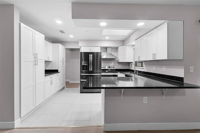 kitchen featuring a breakfast bar, black fridge with ice dispenser, wall chimney range hood, dark stone countertops, and stainless steel range with electric cooktop