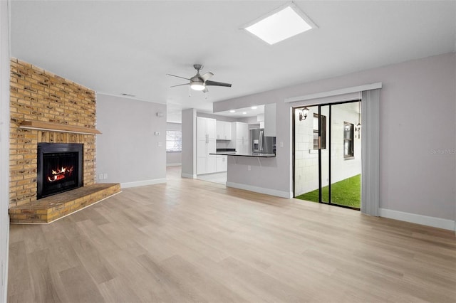 unfurnished living room with light hardwood / wood-style floors, a brick fireplace, and ceiling fan