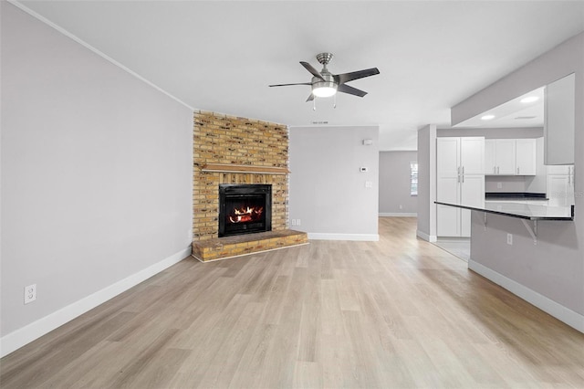 unfurnished living room with ceiling fan, light wood-type flooring, and a brick fireplace