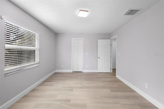 unfurnished bedroom with a textured ceiling, light hardwood / wood-style flooring, and a closet