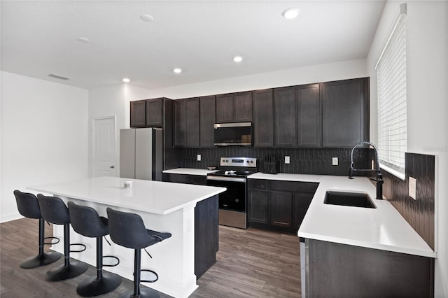 kitchen with appliances with stainless steel finishes, tasteful backsplash, sink, a center island, and dark hardwood / wood-style floors