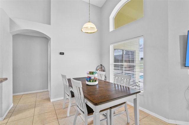 dining space with light tile patterned floors, arched walkways, baseboards, and a towering ceiling