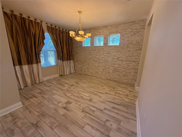 empty room with light wood-type flooring, a textured ceiling, and an inviting chandelier