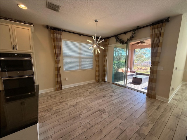 unfurnished dining area featuring ceiling fan with notable chandelier and a textured ceiling