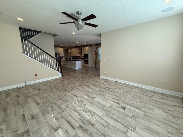 unfurnished living room with a textured ceiling, ceiling fan, and light hardwood / wood-style flooring