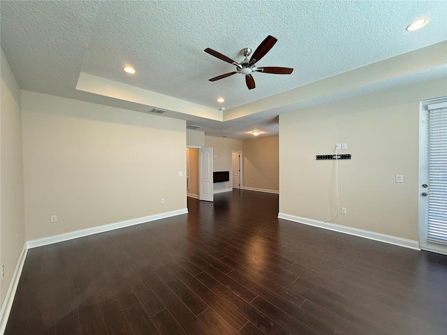 unfurnished living room with a textured ceiling, ceiling fan, a tray ceiling, and dark hardwood / wood-style floors