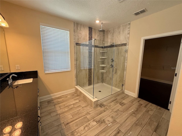 bathroom featuring a textured ceiling, walk in shower, and vanity