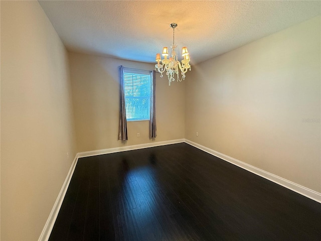 spare room with a textured ceiling, hardwood / wood-style floors, and a notable chandelier