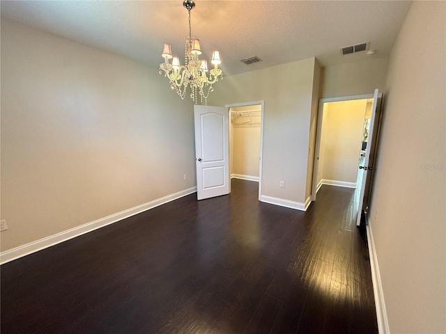 empty room featuring an inviting chandelier and dark wood-type flooring