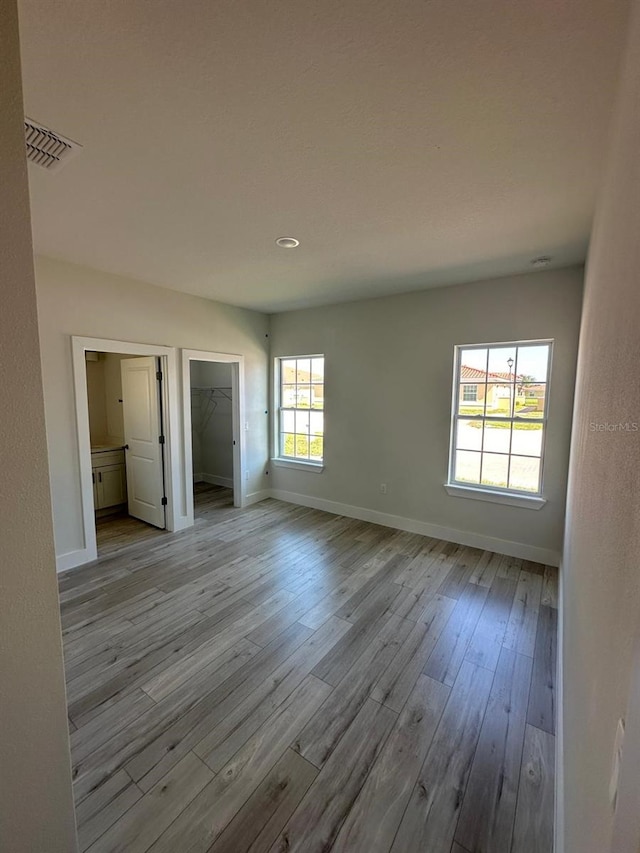 unfurnished bedroom featuring a spacious closet, a closet, and light wood-type flooring