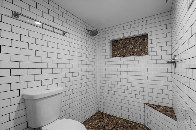 bathroom featuring a tile shower, toilet, and tile walls