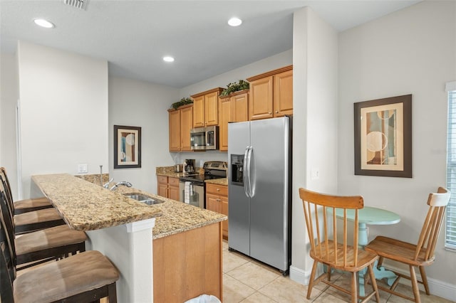 kitchen with appliances with stainless steel finishes, light stone counters, sink, light tile patterned floors, and a breakfast bar area