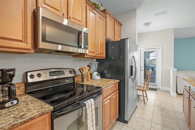 kitchen with appliances with stainless steel finishes, light tile patterned floors, and light stone counters