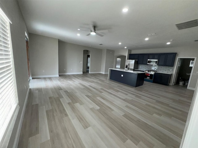 kitchen with stainless steel appliances, hardwood / wood-style floors, ceiling fan, backsplash, and a center island with sink