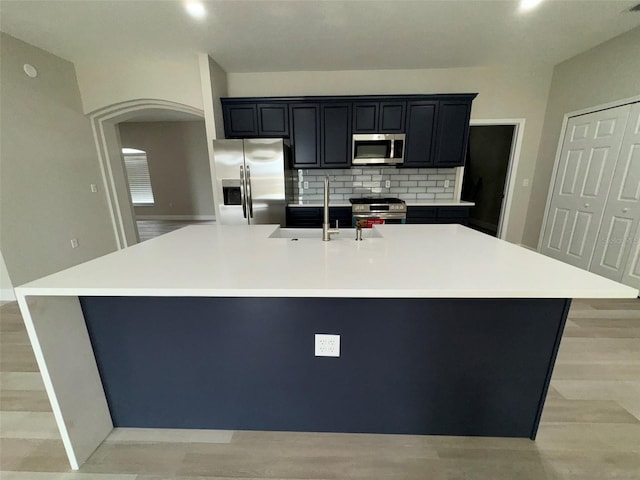 kitchen with decorative backsplash, a large island, light wood-type flooring, appliances with stainless steel finishes, and sink