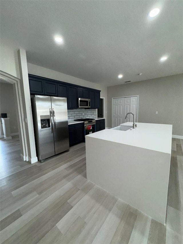 kitchen with a center island with sink, light wood-type flooring, backsplash, appliances with stainless steel finishes, and sink