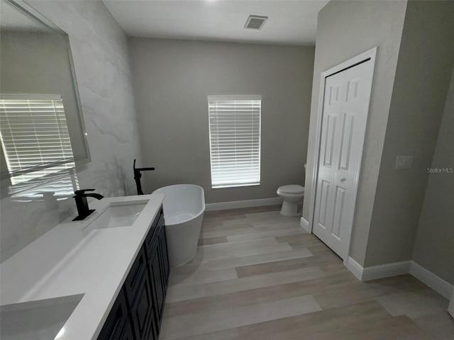 bathroom with a tub to relax in, toilet, vanity, and wood-type flooring