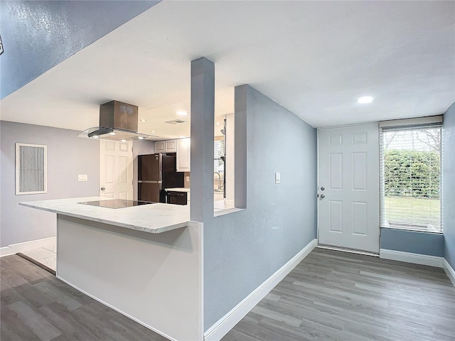 kitchen featuring kitchen peninsula, light hardwood / wood-style floors, island exhaust hood, black appliances, and white cabinetry