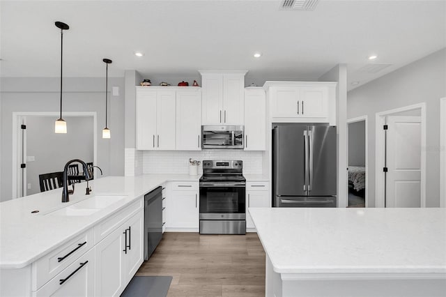 kitchen with sink, stainless steel appliances, white cabinetry, and pendant lighting