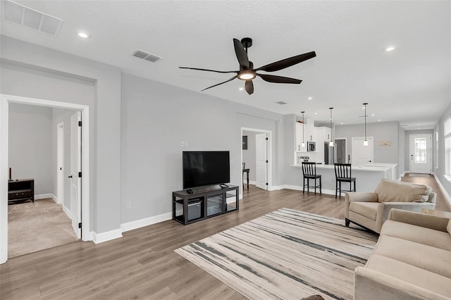 living room featuring ceiling fan, a textured ceiling, and light hardwood / wood-style flooring