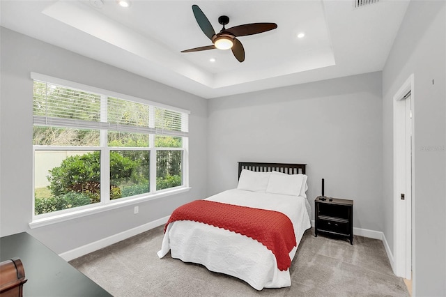 bedroom featuring ceiling fan, light carpet, and a tray ceiling