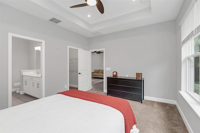 carpeted bedroom with a spacious closet, ensuite bath, a closet, a raised ceiling, and ceiling fan