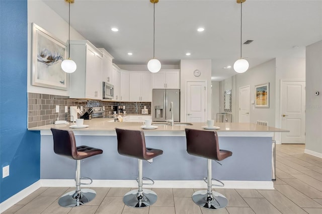 kitchen featuring decorative light fixtures, tasteful backsplash, white cabinetry, appliances with stainless steel finishes, and a breakfast bar area