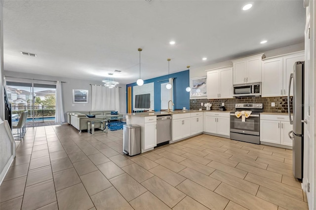 kitchen featuring kitchen peninsula, stainless steel appliances, decorative light fixtures, and white cabinetry