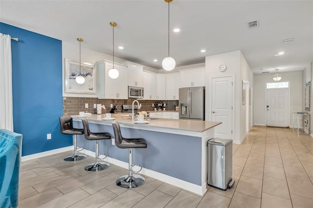 kitchen featuring decorative light fixtures, a kitchen bar, white cabinets, appliances with stainless steel finishes, and sink