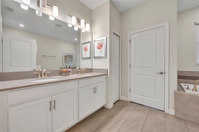 bathroom with a relaxing tiled tub, vanity, and tile patterned floors