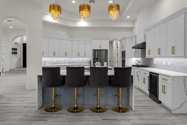 kitchen with wine cooler, white cabinetry, pendant lighting, stainless steel appliances, and a kitchen island with sink