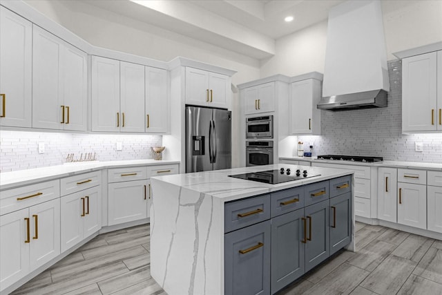 kitchen with white cabinetry, stainless steel appliances, light stone counters, and wall chimney range hood