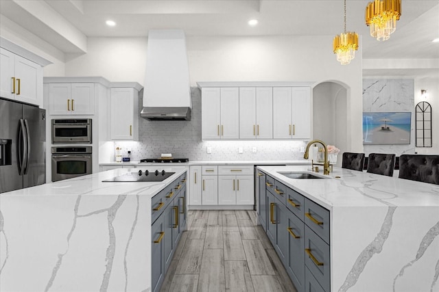 kitchen with sink, light stone counters, white cabinets, decorative light fixtures, and wall chimney exhaust hood