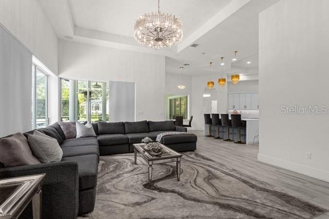 living room featuring an inviting chandelier, a tray ceiling, wood-type flooring, and a towering ceiling